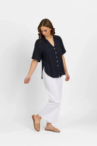 Woman wearing a navy short-sleeve button-up shirt with white wide-leg pants and tan slides
