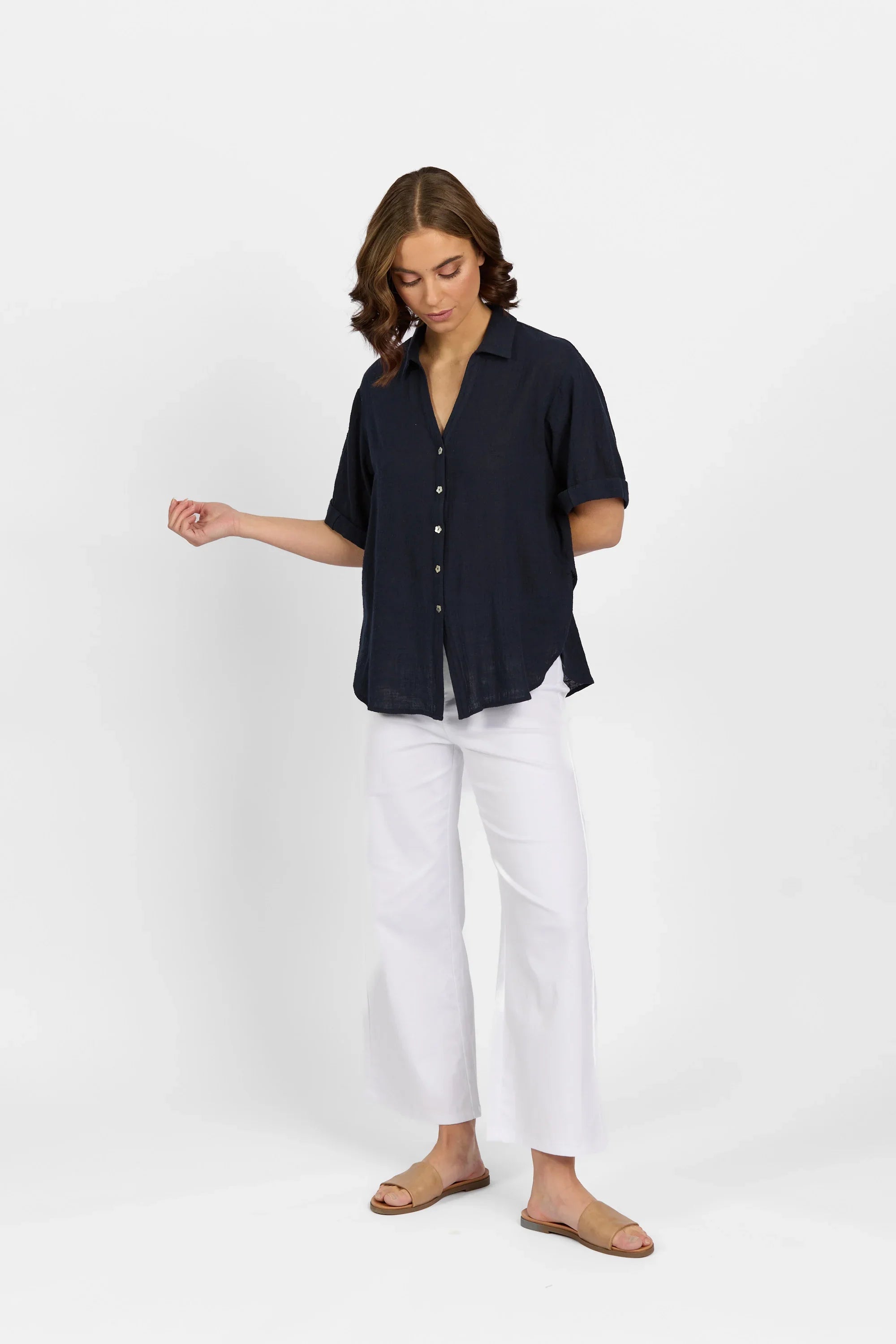 Woman wearing a navy button-up short sleeve shirt with white wide-leg pants and tan sandals