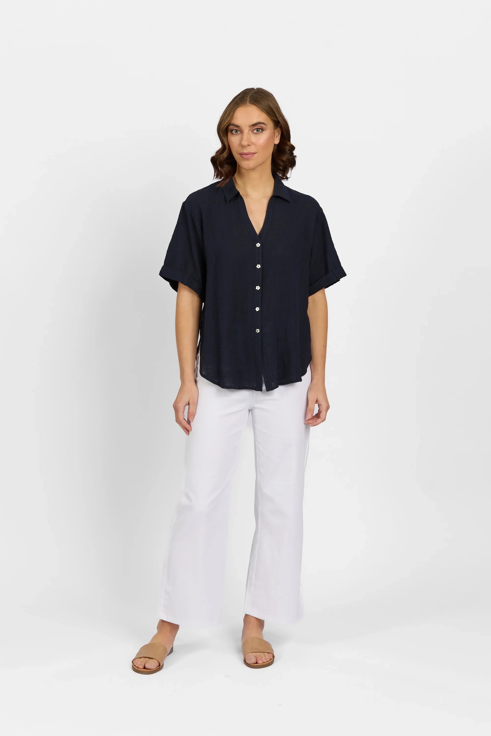 Woman wearing short sleeve navy button-up shirt and white flare pants, studio background