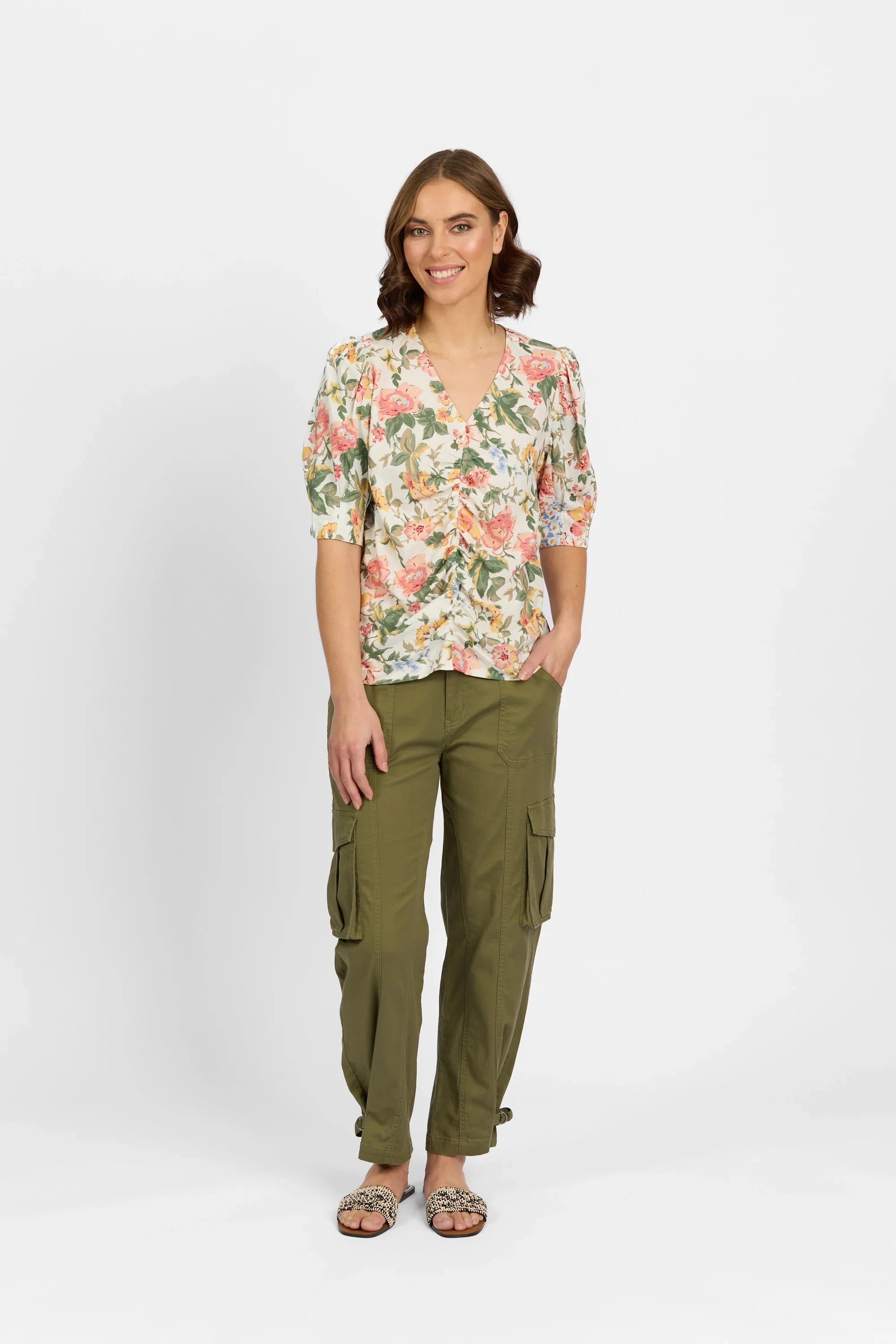 Woman in floral ruched blouse with half sleeves and olive green cargo pants, standing indoors