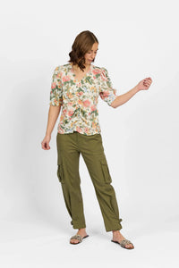 Woman wearing a floral v-neck blouse with puff sleeves and olive cargo pants against white background.