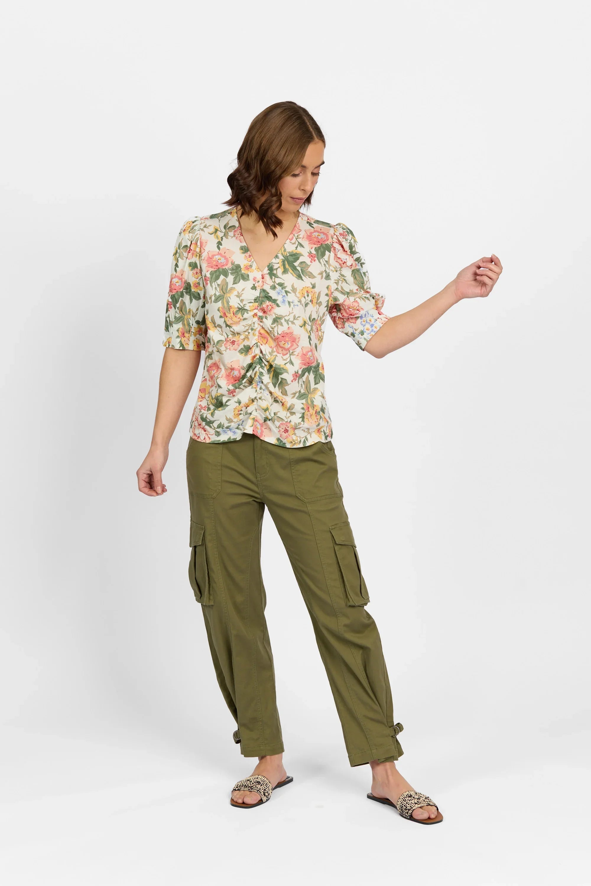 Woman wearing a floral v-neck blouse with puff sleeves and olive cargo pants against white background.