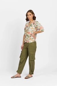 Woman wearing floral puff sleeve blouse, olive green cargo pants and sandals, studio background
