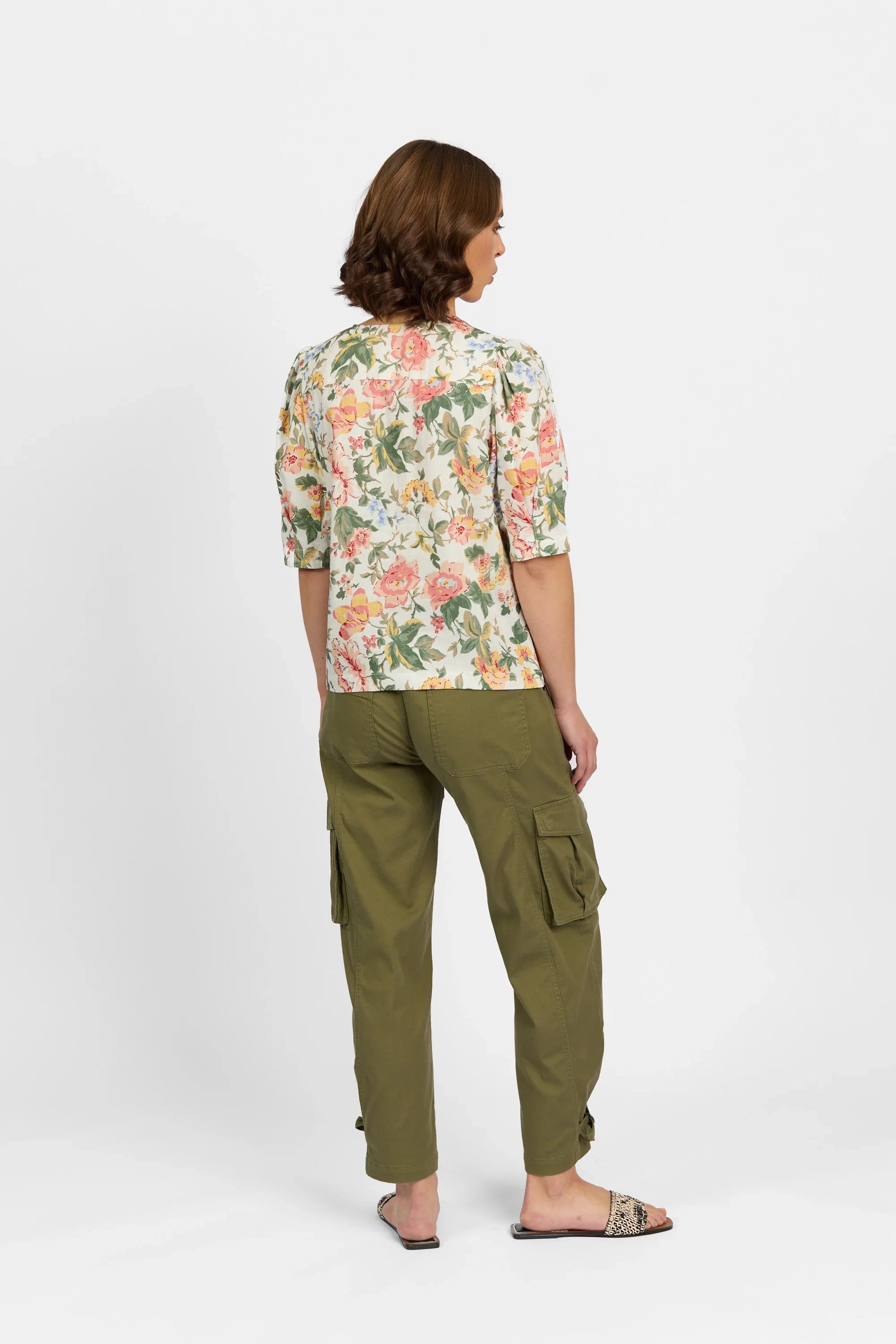 Woman in floral print top and olive green cargo pants, standing on white background