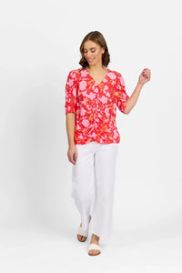 Woman wearing a vibrant pink floral top with ruched front, white wide-leg pants, and sandals