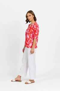 Woman wearing a bright floral top with white wide-leg pants and slide sandals