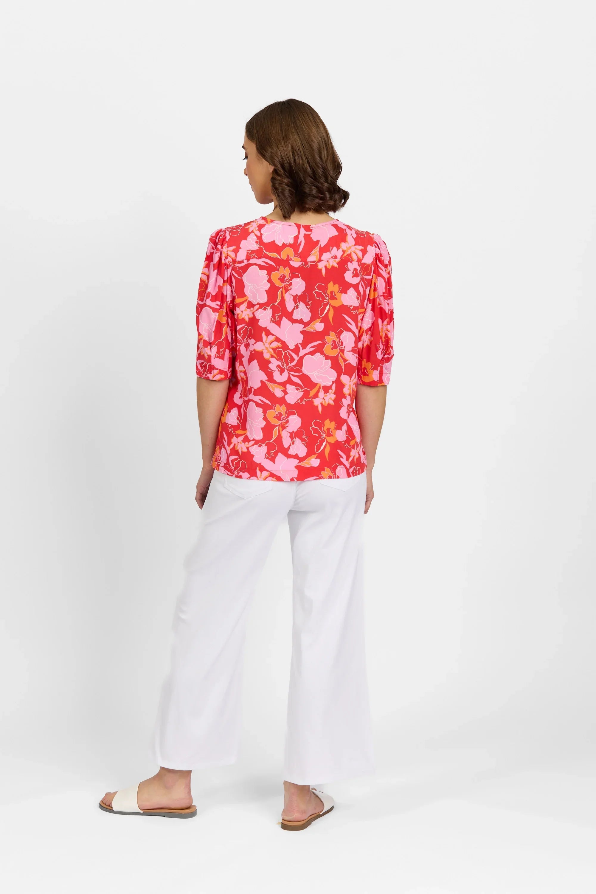 Woman wearing a pink floral blouse with puff sleeves and white wide-leg pants, back view