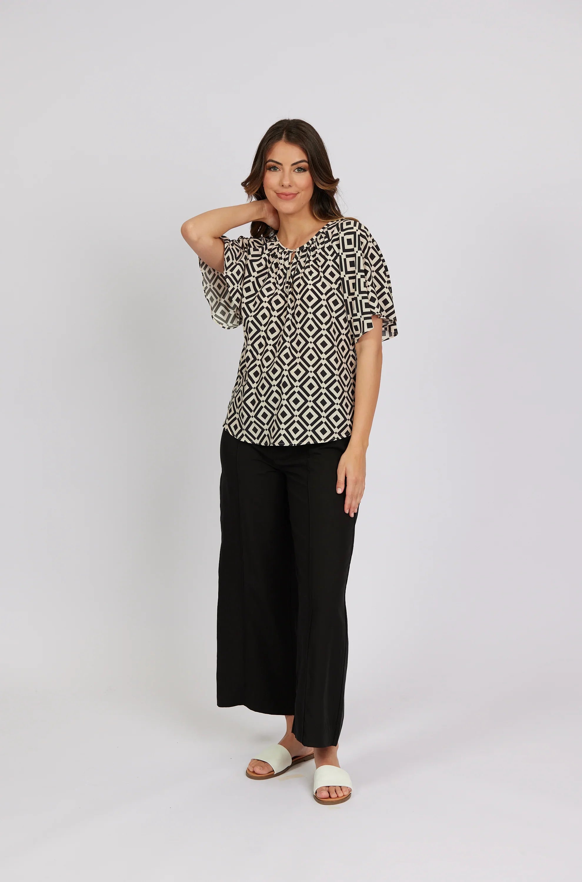 Woman wearing geometric print short-sleeve top with black wide-leg pants and sandals