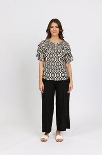 Woman wearing a geometric print blouse, black wide-leg pants, and white sandals