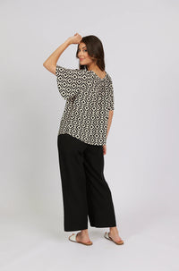 Woman wearing a geometric patterned top with black wide-leg pants and white sandals
