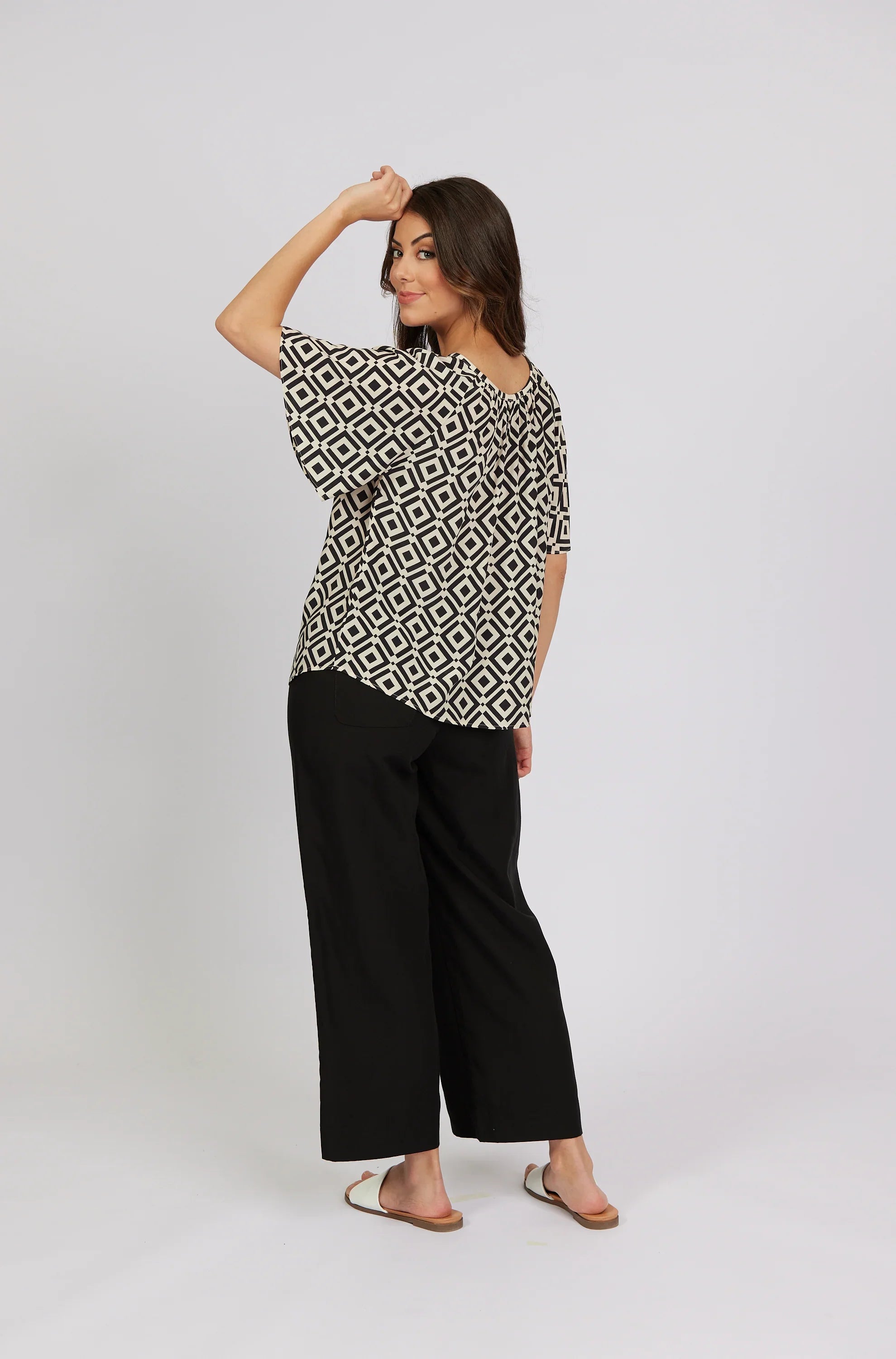 Woman wearing a geometric patterned top with black wide-leg pants and white sandals
