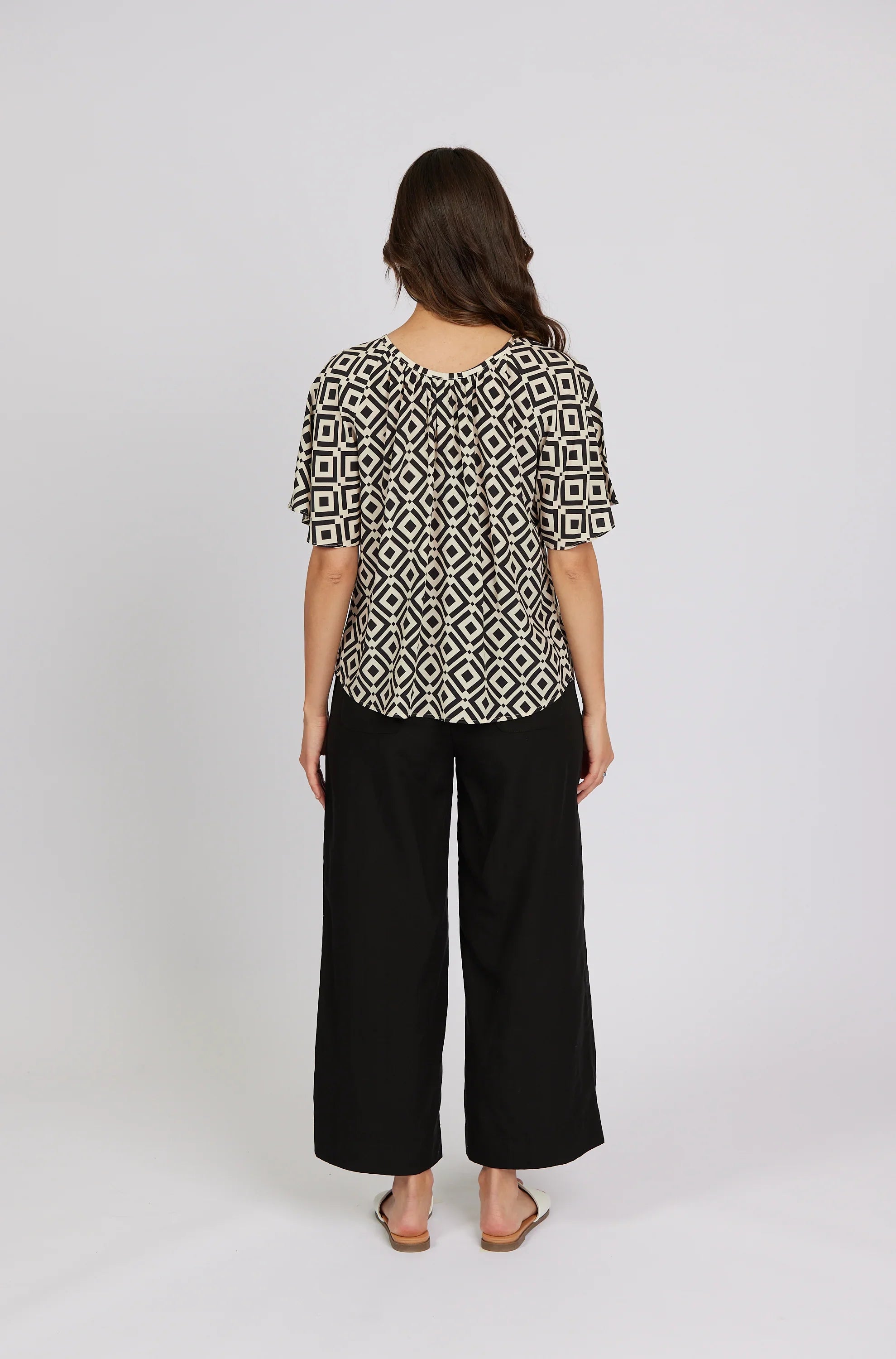 Woman wearing geometric print short sleeve top and black wide leg pants, back view