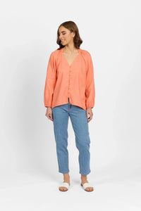 Woman wearing coral long sleeve V-neck shirt with button front, blue jeans, and slide sandals
