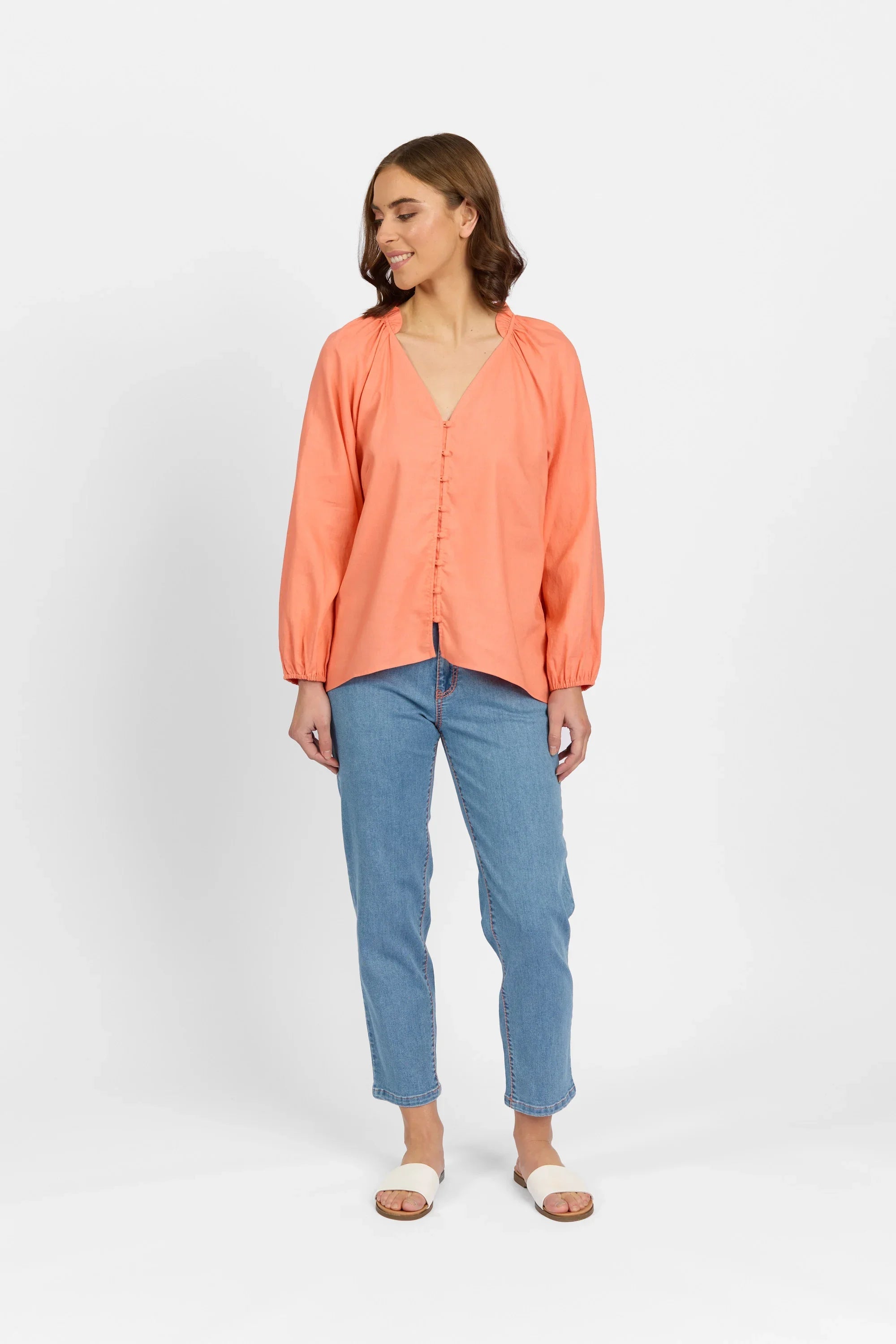 Woman wearing coral long sleeve V-neck shirt with button front, blue jeans, and slide sandals