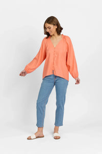 Woman wearing coral long sleeve button-up blouse with blue jeans and sandals