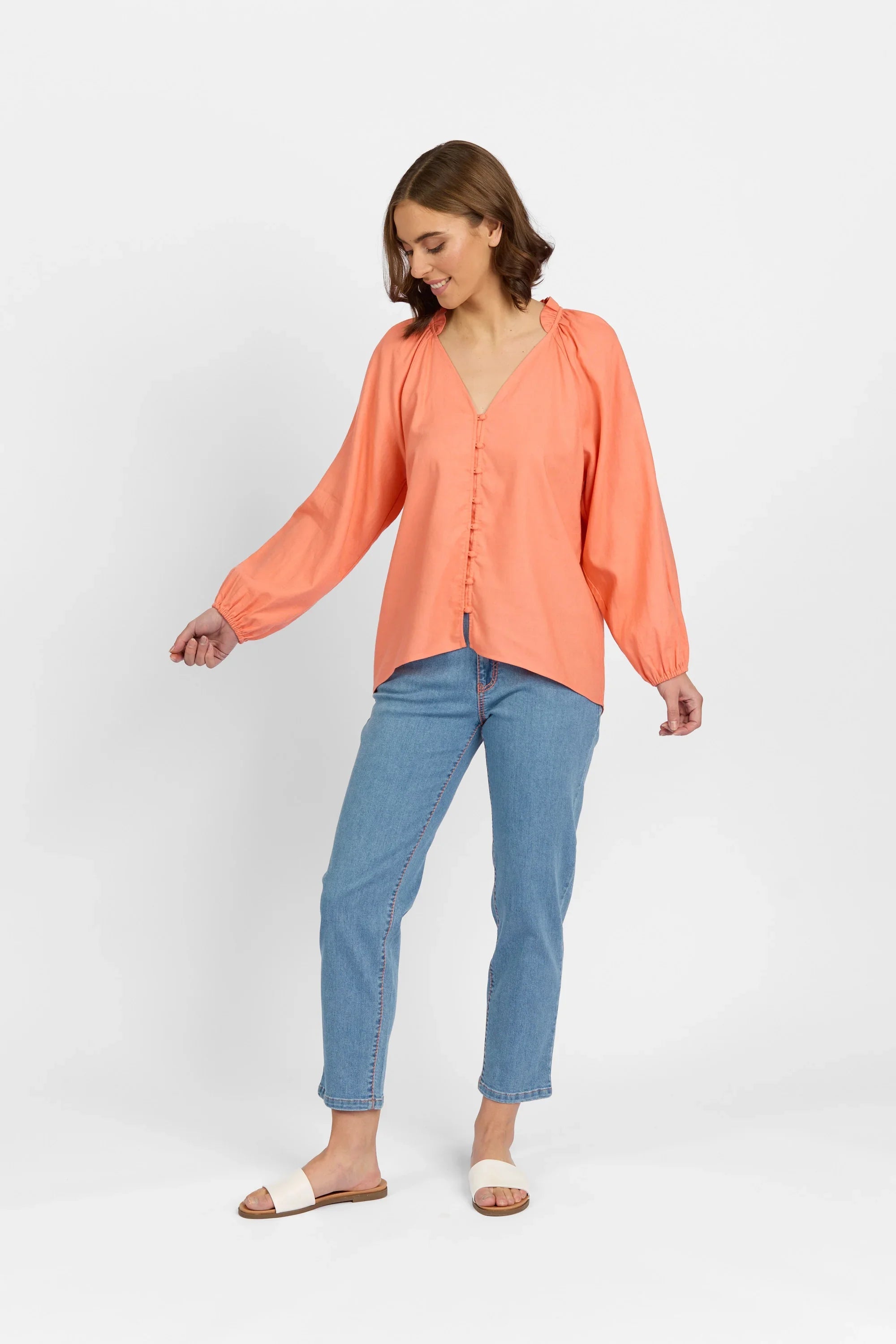 Woman wearing coral long sleeve button-up blouse with blue jeans and sandals