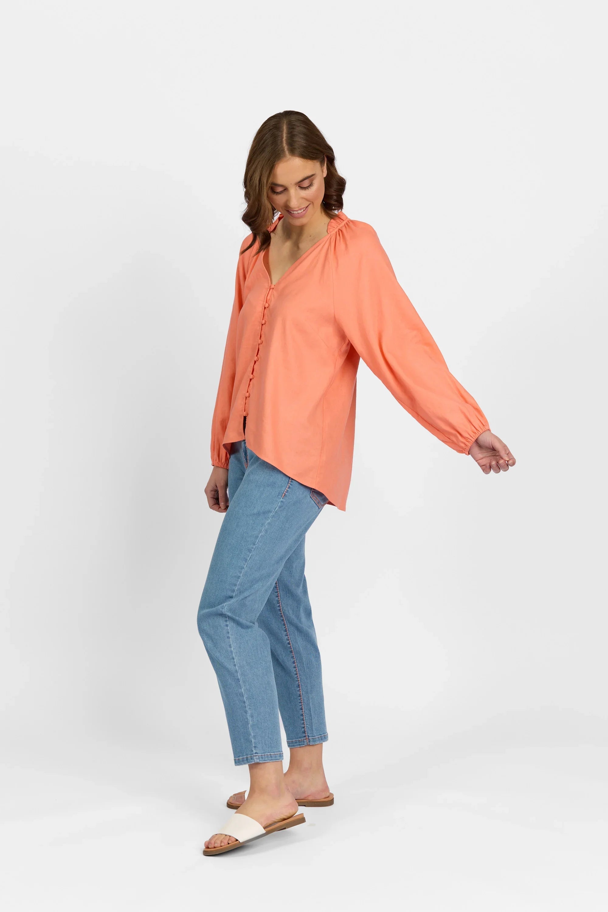 Woman wearing coral button-up long sleeve shirt with blue jeans and white slide sandals