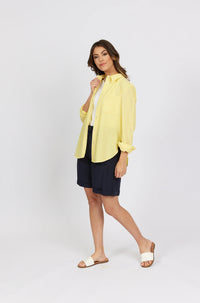 Woman wearing lemon yellow striped button-up shirt, navy shorts, and white slide sandals