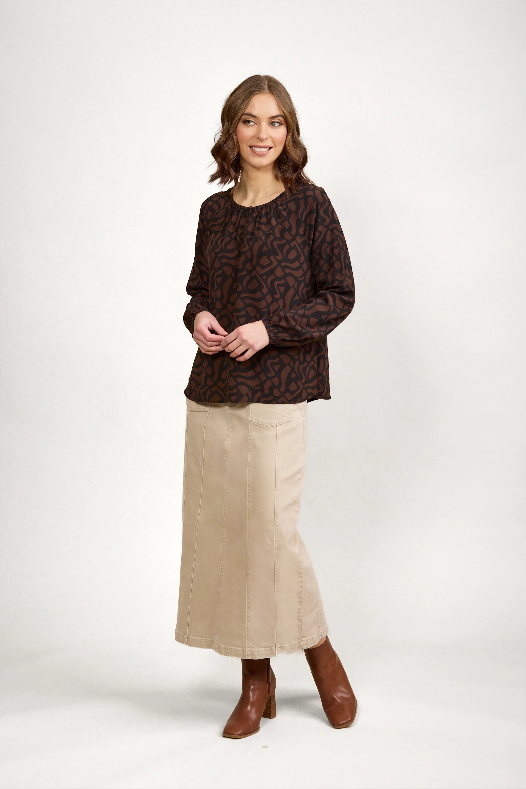 Woman wearing abstract print mocha top, beige maxi skirt, and brown ankle boots