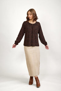 Woman in patterned brown long-sleeve blouse, beige maxi skirt, and brown ankle boots