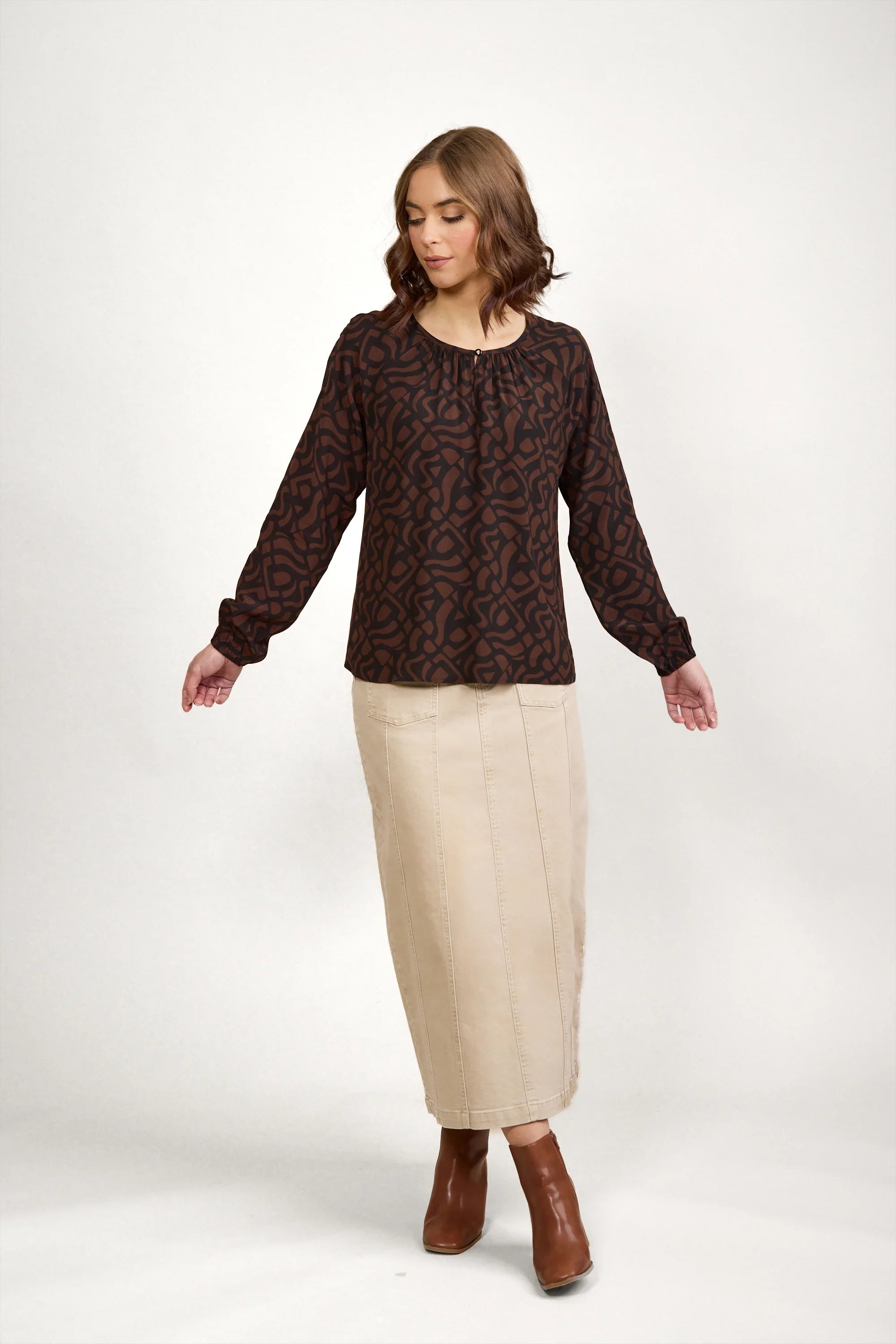 Woman in patterned brown long-sleeve blouse, beige maxi skirt, and brown ankle boots
