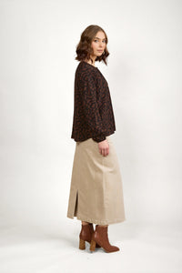 Woman in brown patterned top, beige maxi skirt, and brown ankle boots on white background