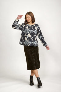 Woman in a long sleeve abstract print blouse, button front midi skirt, and black ankle boots