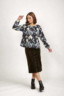 Woman in a long sleeve abstract print blouse, button front midi skirt, and black ankle boots