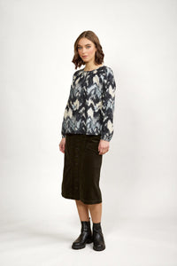Woman wearing abstract print long sleeve blouse, olive button-front midi skirt, black boots