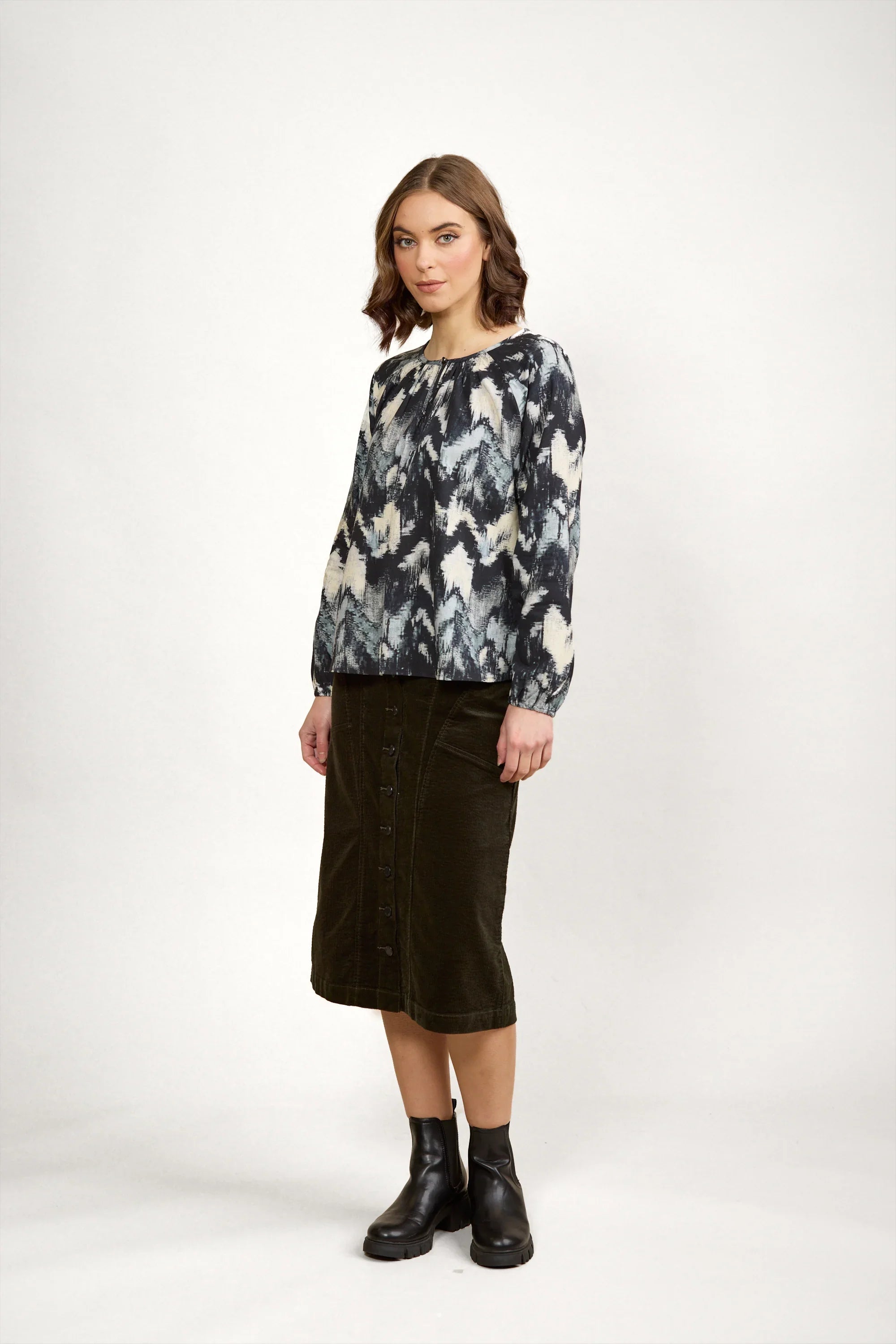 Woman wearing abstract print long sleeve blouse, olive button-front midi skirt, black boots