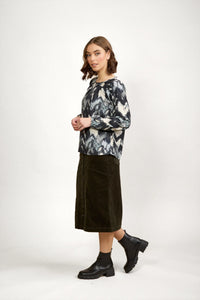 Woman in abstract print long sleeve top, dark midi skirt, and black ankle boots