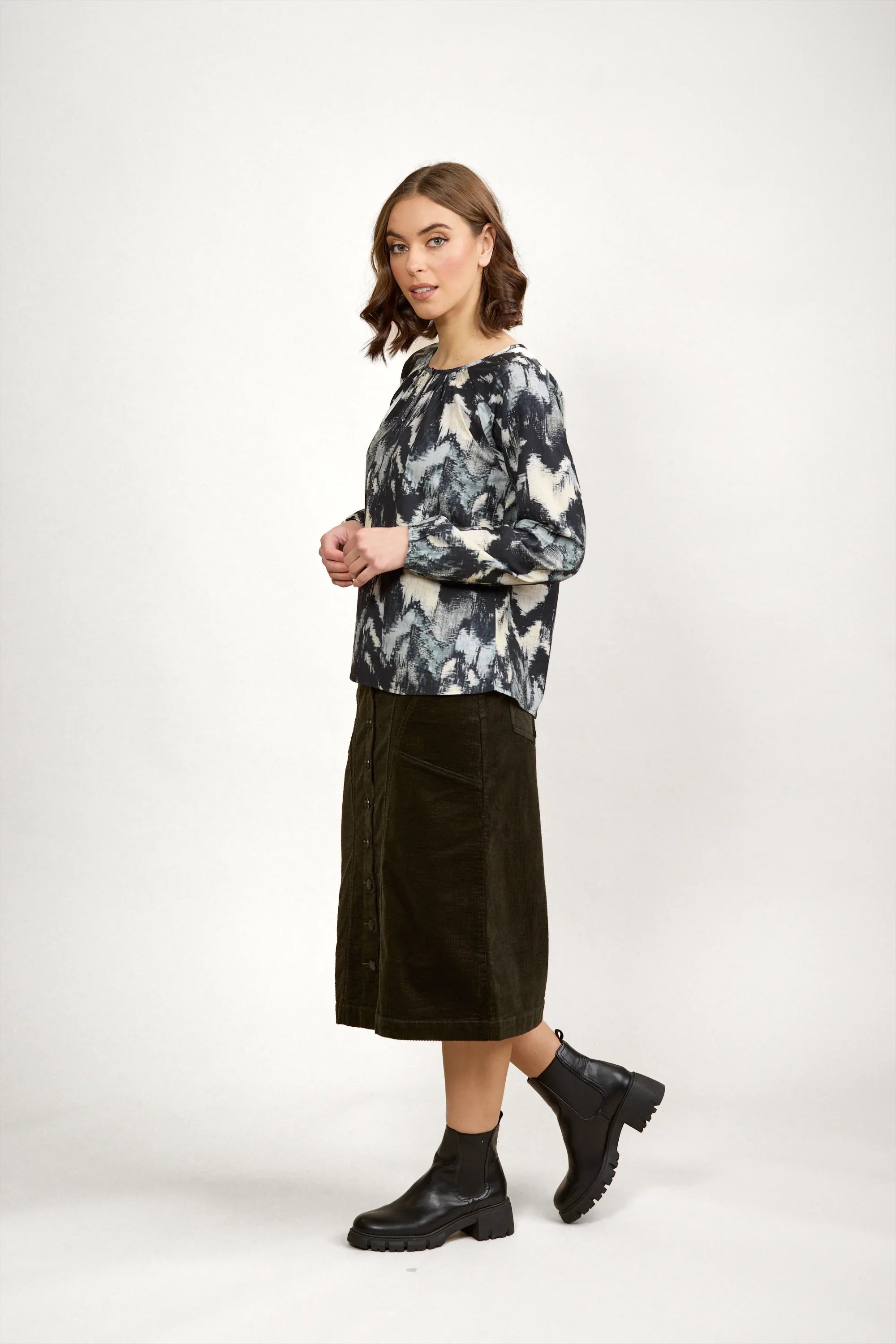 Woman in abstract print long sleeve top, dark midi skirt, and black ankle boots
