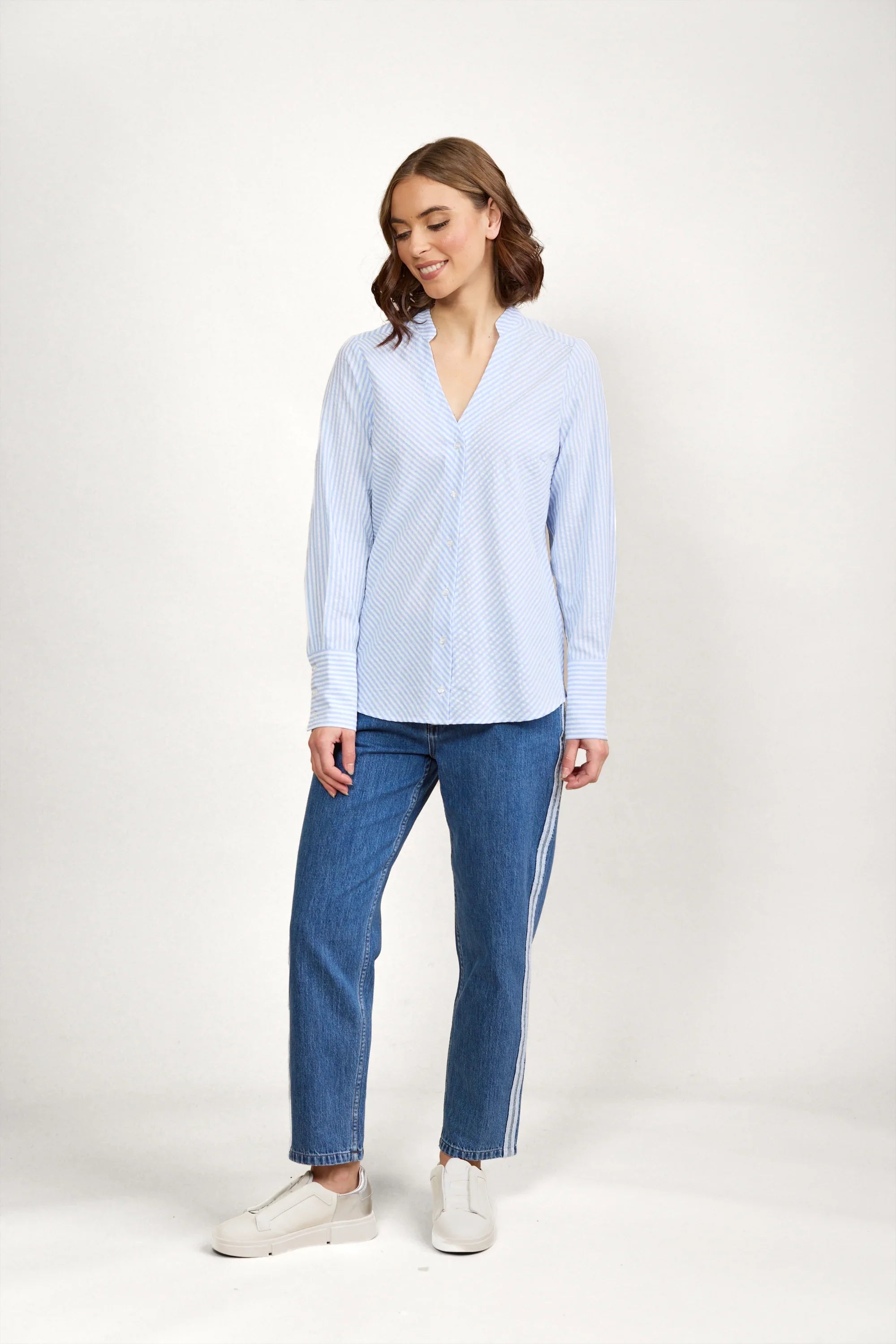 Woman wearing blue and white striped button-up shirt, jeans, and white sneakers