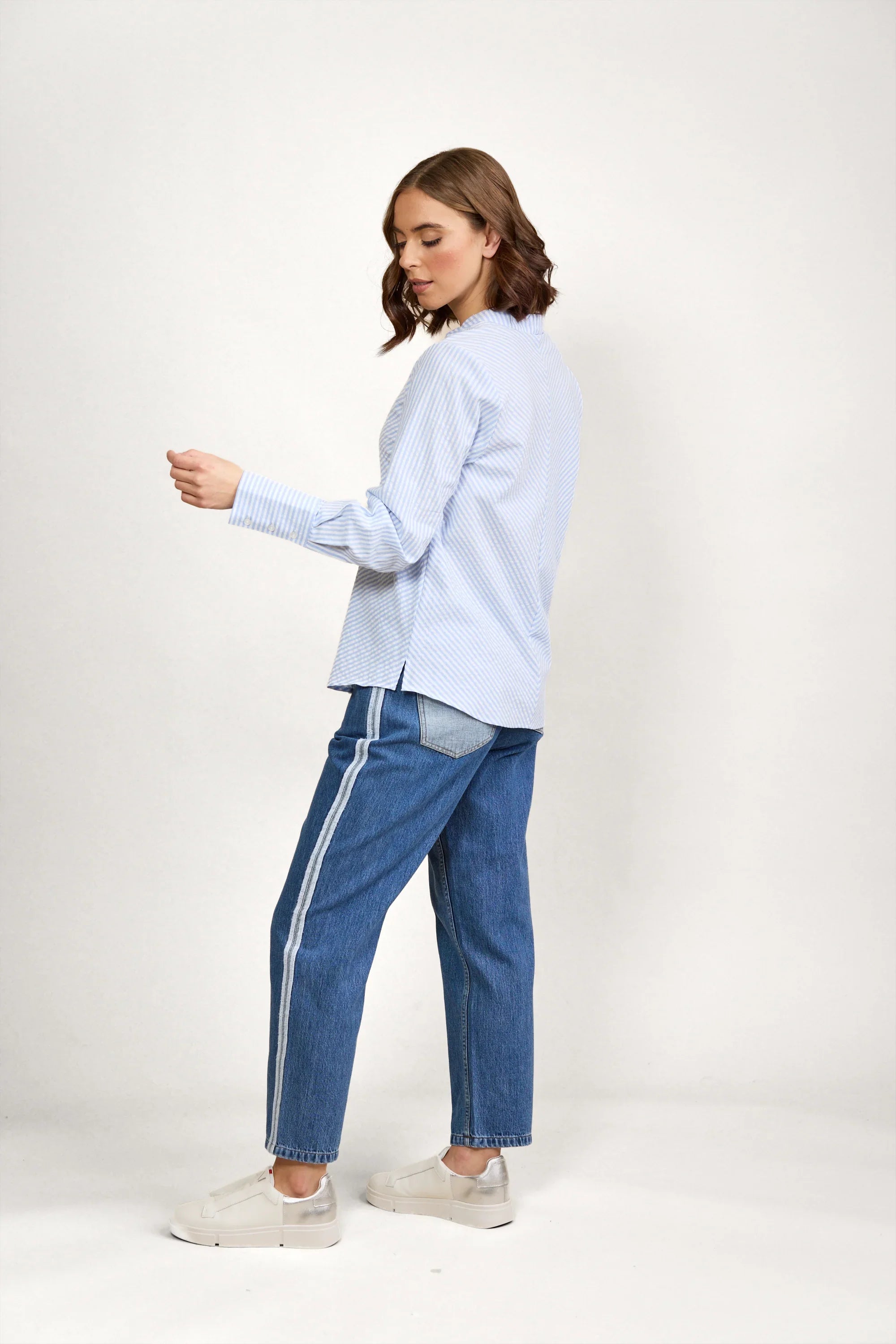 Woman wearing a blue and white striped long sleeve shirt and blue jeans with side stripes