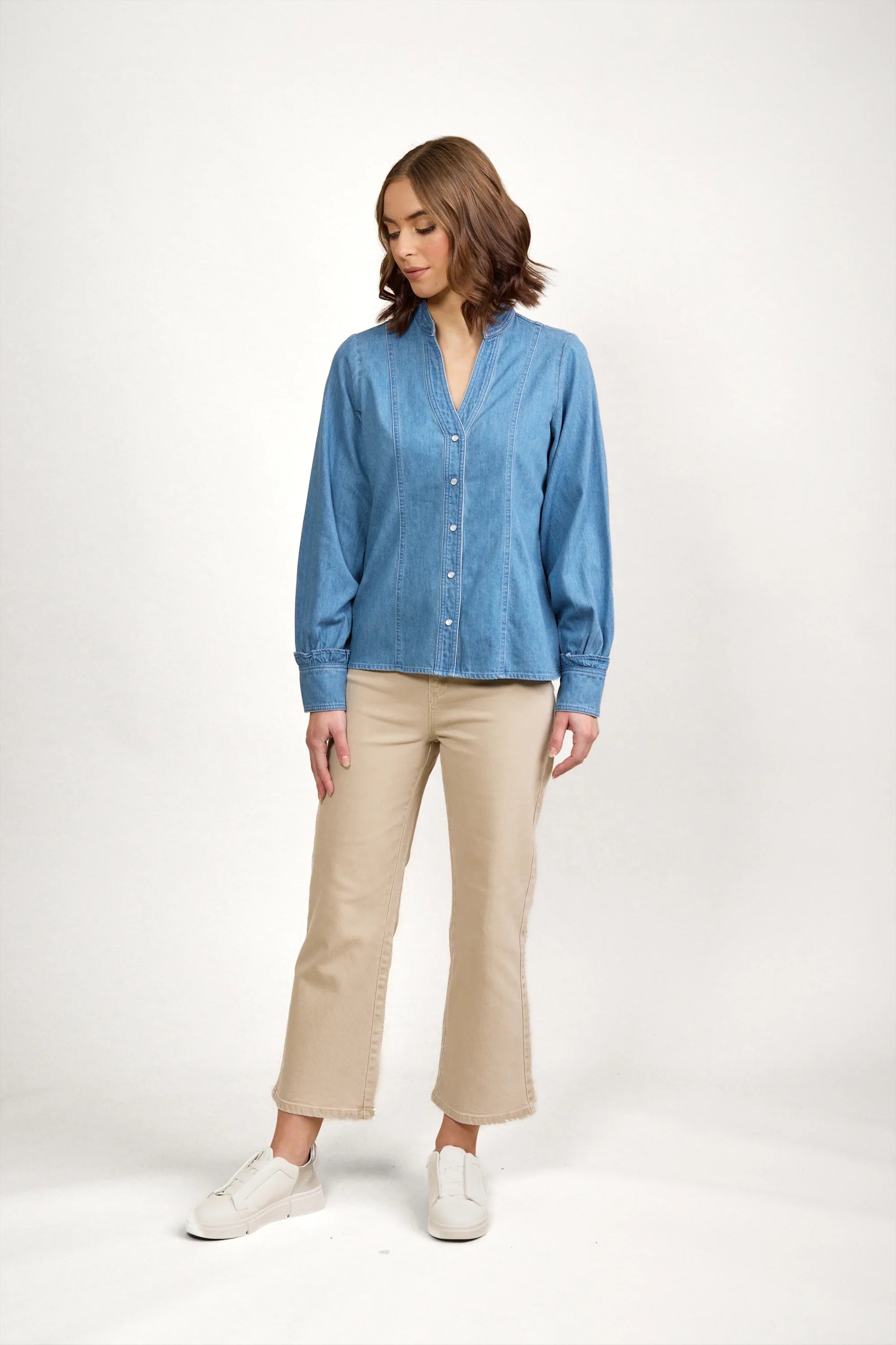 Woman modeling blue denim shirt with buttons, beige cropped pants, and white sneakers