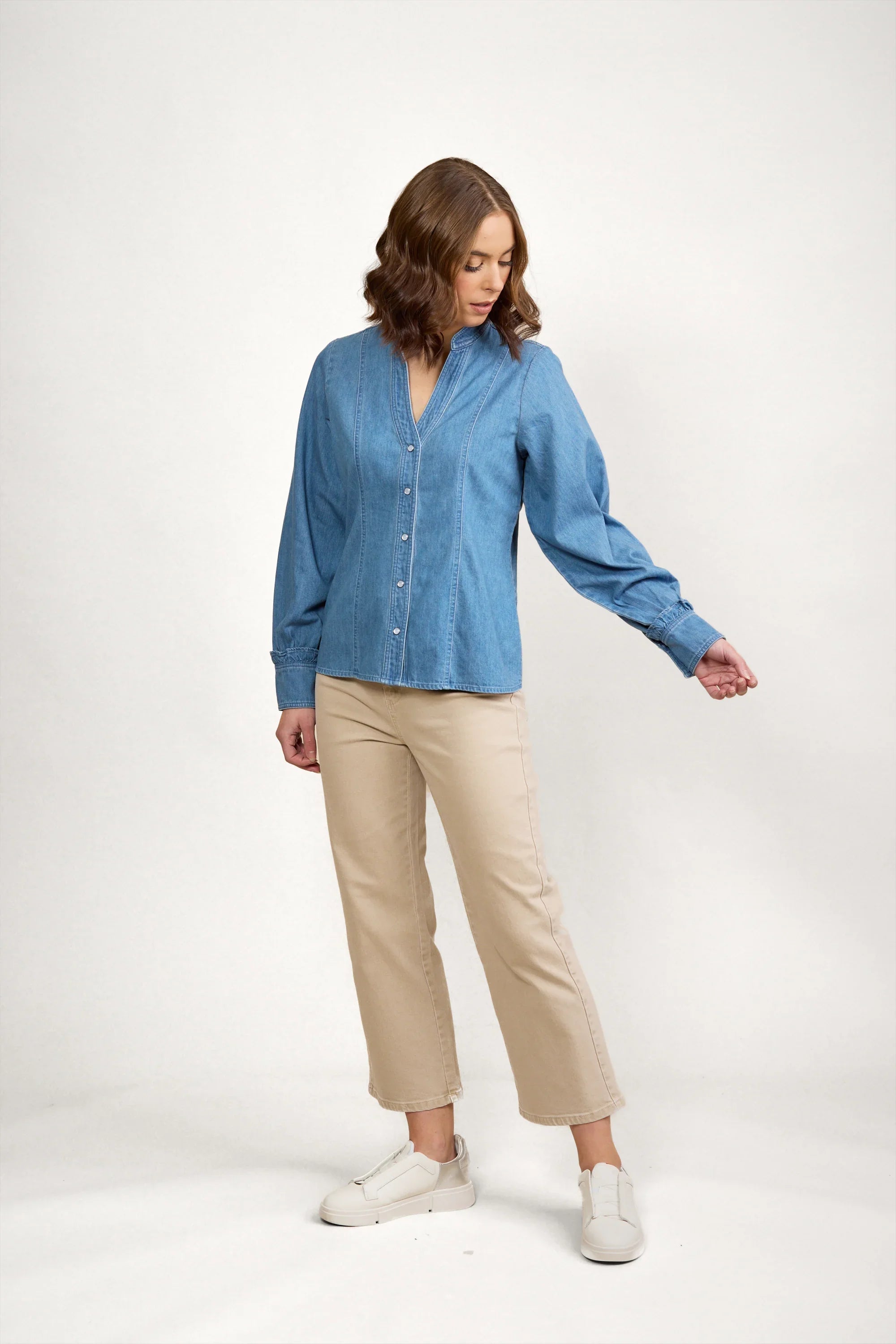 Woman modeling a blue denim shirt with button front and long sleeves, paired with beige pants