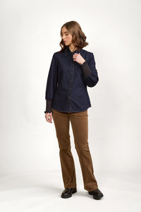 Woman wearing a dark denim button-up shirt with smocked cuffs and brown corduroy pants