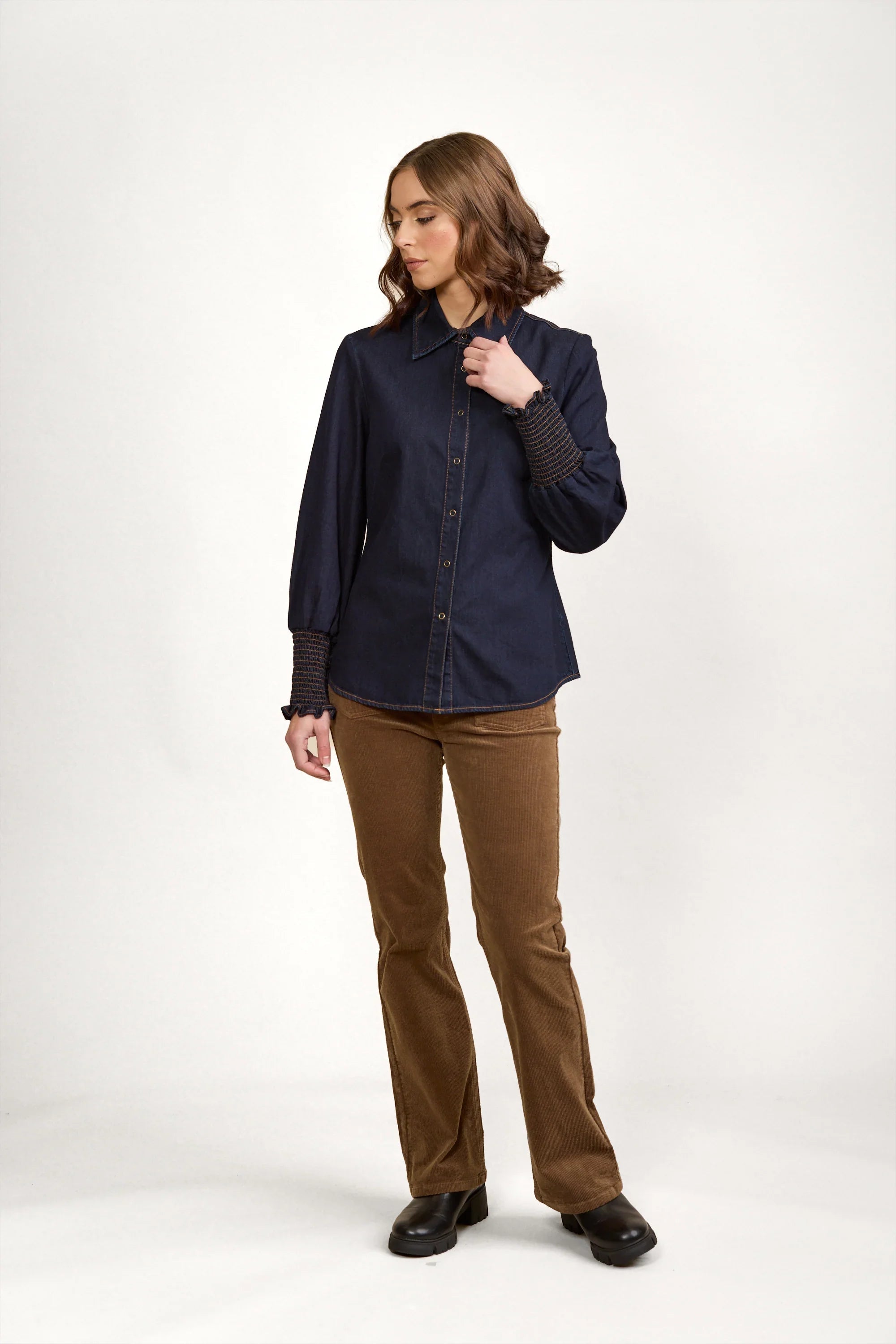Woman wearing a dark denim button-up shirt with smocked cuffs and brown corduroy pants