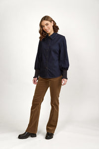 Woman in dark denim button-up shirt with balloon sleeves, brown corduroy pants, black boots