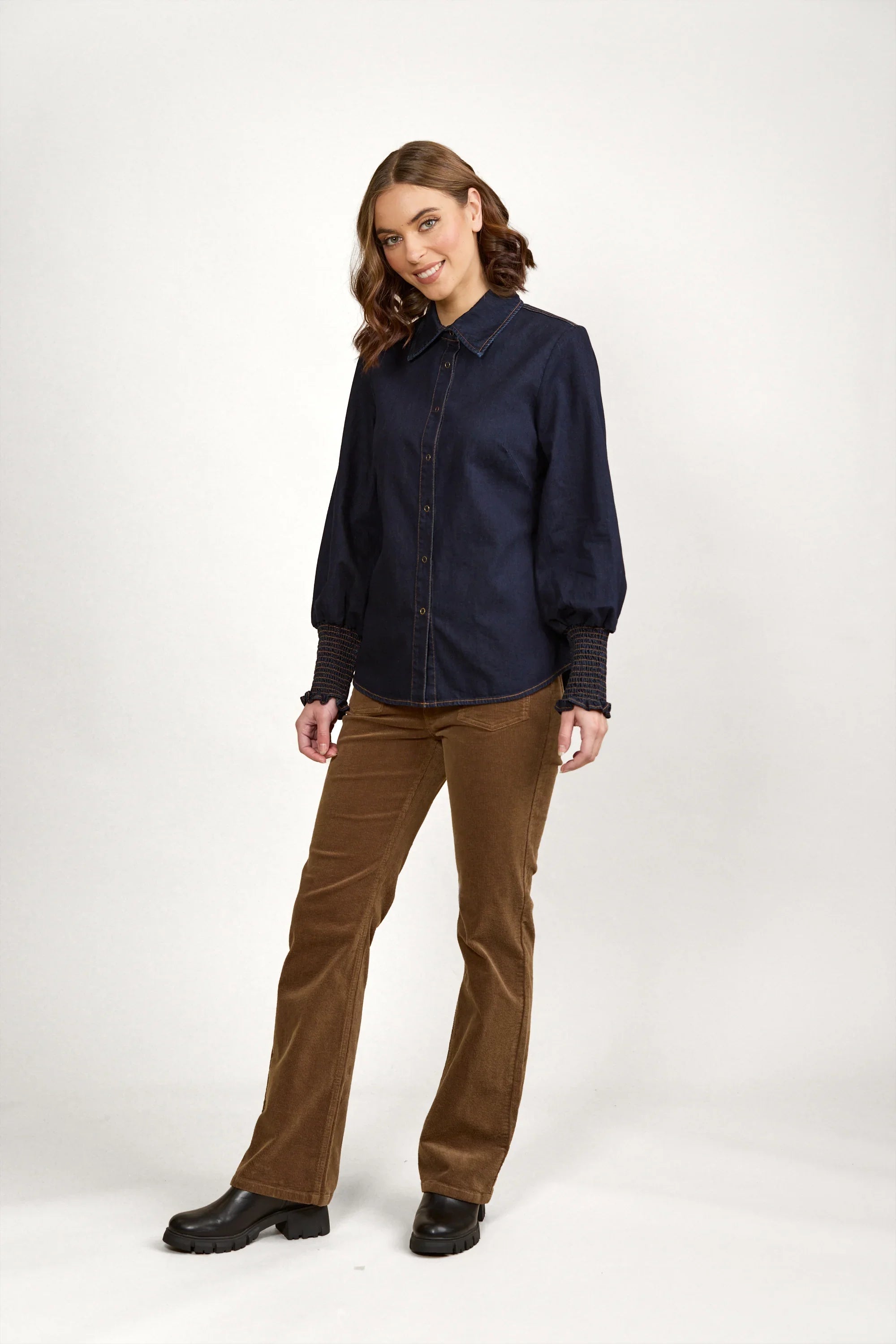 Woman in dark denim button-up shirt with balloon sleeves, brown corduroy pants, black boots