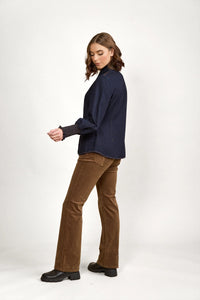 Woman wearing dark denim shirt, brown corduroy pants, and black boots on white background
