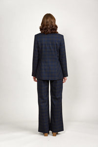 Back view of woman in navy check plaid blazer and wide-leg pants, studio background