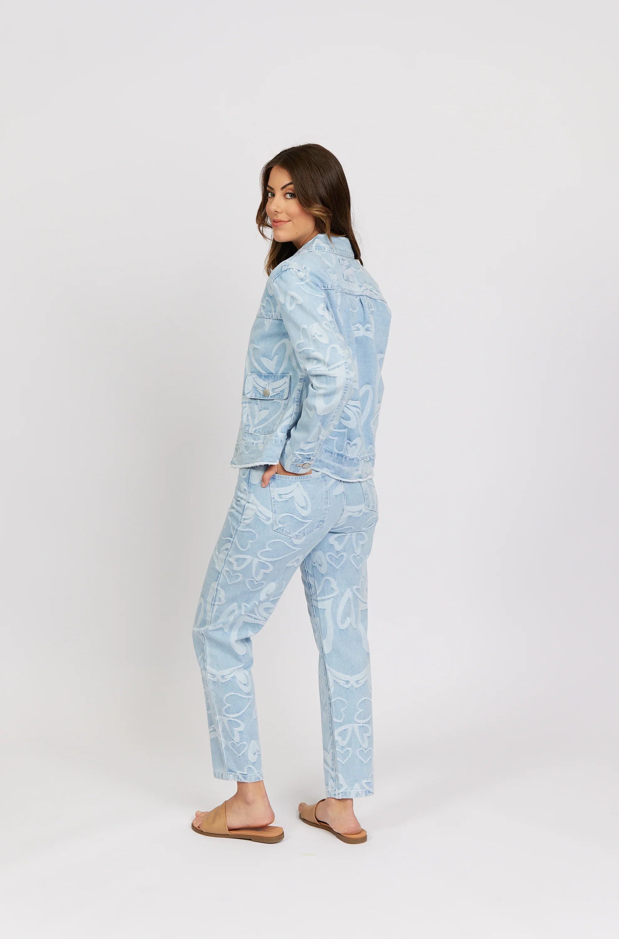 Woman modeling light blue denim jacket and jeans with white heart pattern, casual fashion.