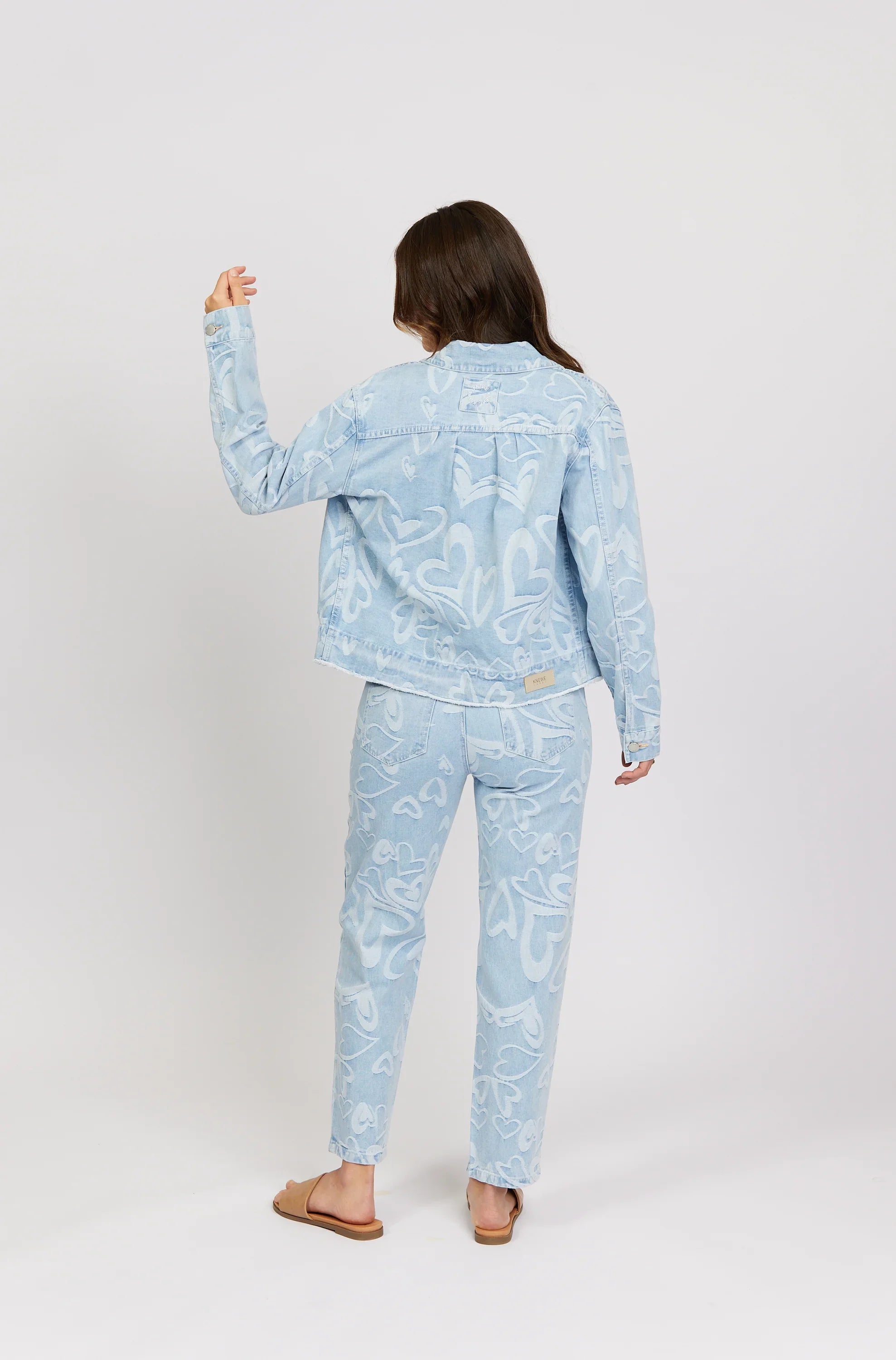 Woman wearing light blue denim jacket and jeans with white heart patterns, back view