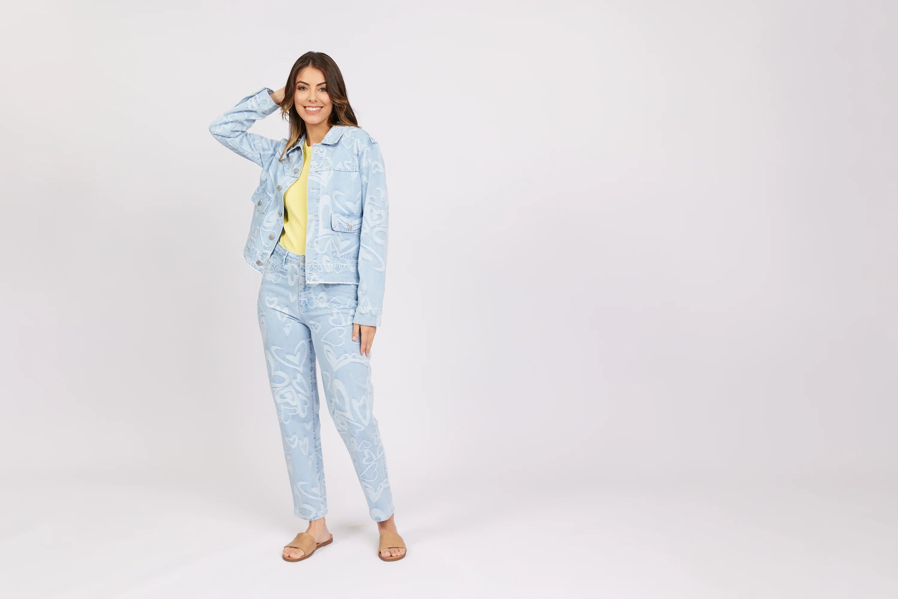 Woman modeling light blue denim jacket and jeans with white heart patterns, yellow top, sandals
