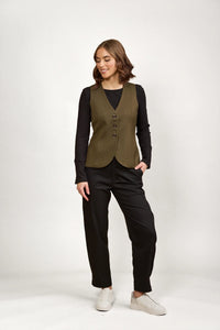 Woman wearing an olive green buttoned vest over black long sleeve top and black pants