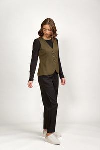 Woman wearing an olive green buttoned vest, black long sleeve top, black pants, and white sneakers