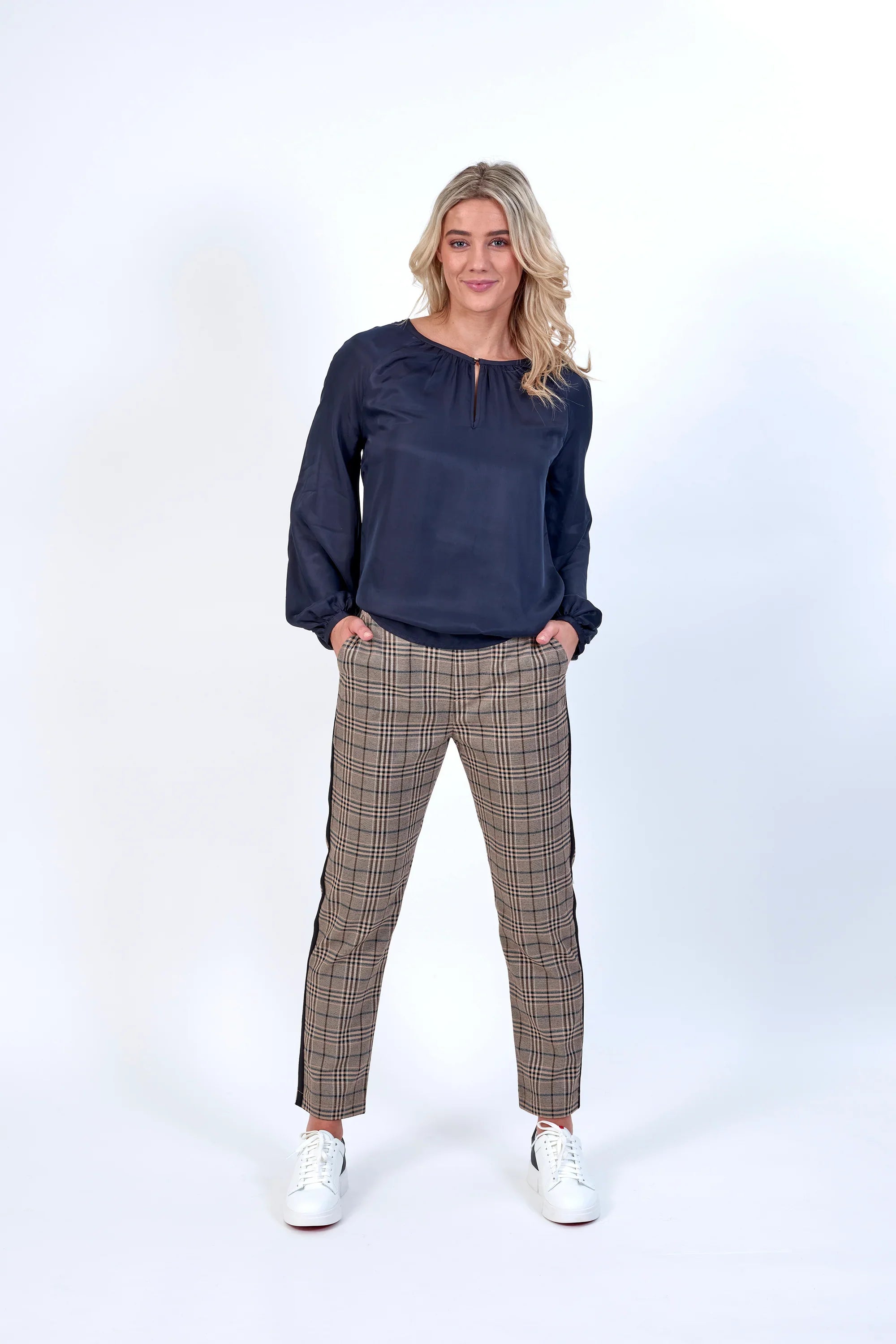 Woman wearing black blouse and plaid check pants with white sneakers on white background