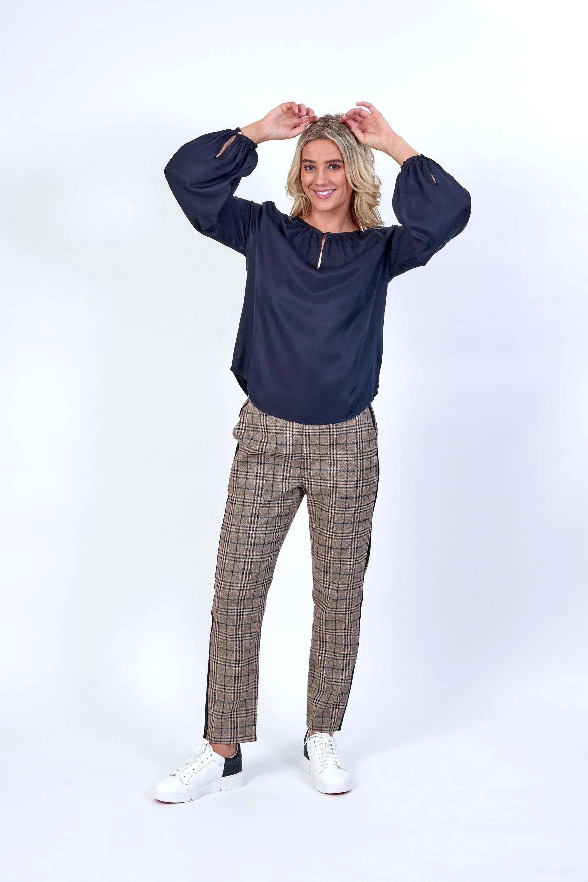 Woman wearing navy blouse and checked straight-leg pants with white sneakers, studio background