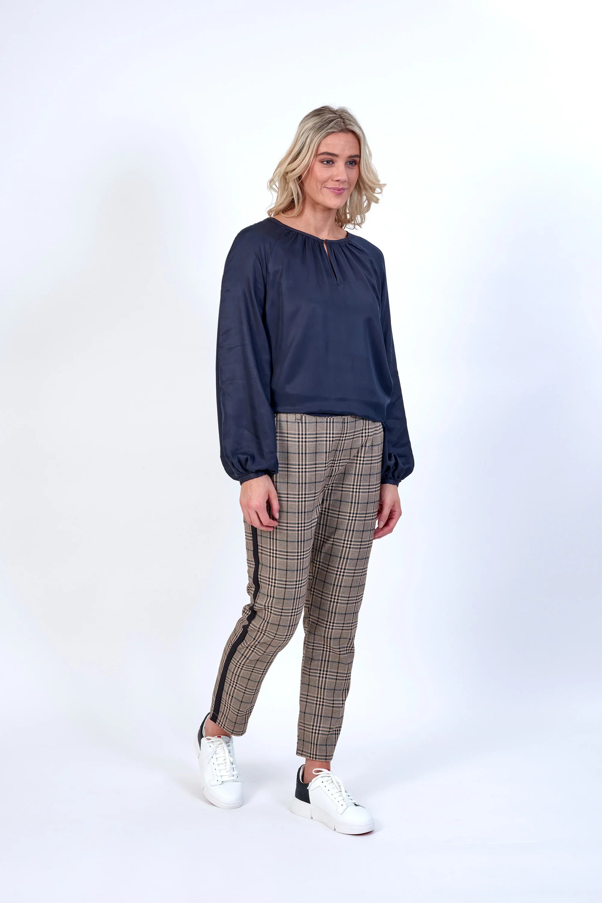 Woman wearing a navy long-sleeve blouse and checked tapered pants with white sneakers